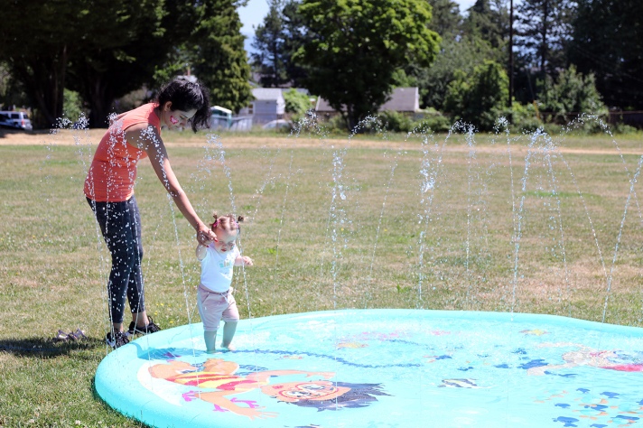 A baby walks on a splash pad in a park.